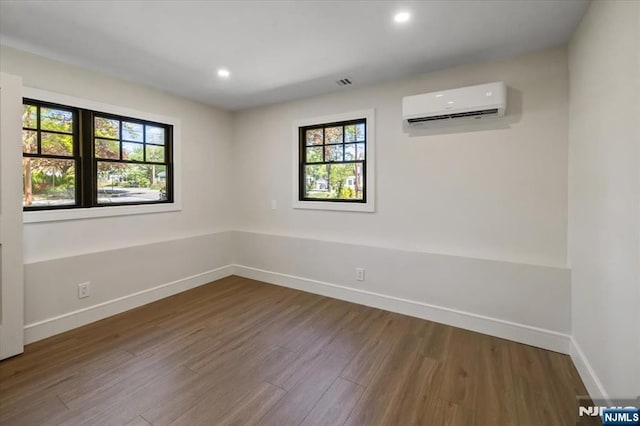 empty room with a wall mounted air conditioner, plenty of natural light, wood finished floors, baseboards, and recessed lighting