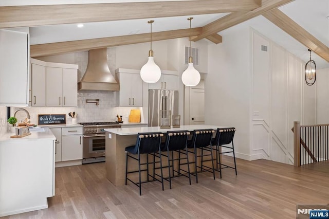 kitchen featuring premium appliances, a sink, premium range hood, decorative backsplash, and a breakfast bar