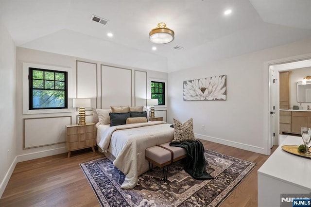bedroom featuring wood finished floors, baseboards, vaulted ceiling, and connected bathroom