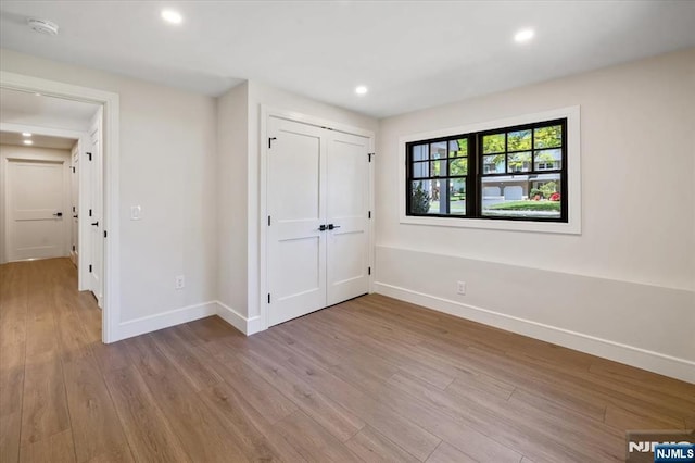 unfurnished bedroom featuring baseboards, wood finished floors, recessed lighting, and a closet