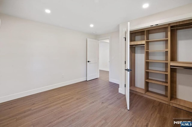 unfurnished bedroom featuring wood finished floors, baseboards, recessed lighting, and a closet