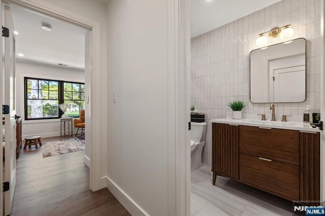 bathroom featuring tile walls, toilet, vanity, wood finished floors, and baseboards
