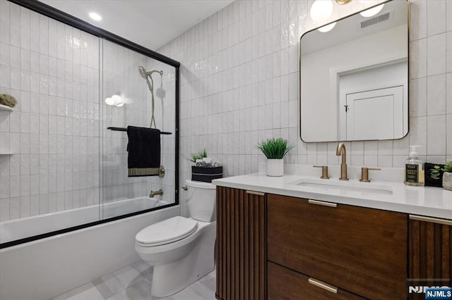 bathroom featuring tile walls, vanity, toilet, shower / bath combination with glass door, and tasteful backsplash