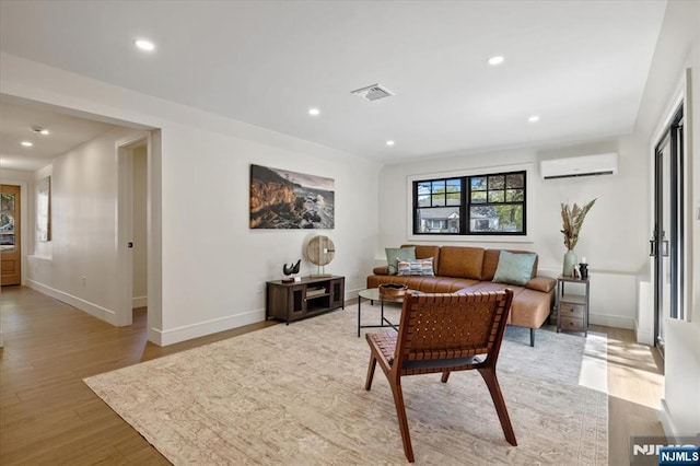 living area featuring a wall unit AC, light wood-type flooring, baseboards, and recessed lighting