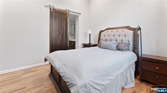 bedroom with connected bathroom, a barn door, and light hardwood / wood-style floors