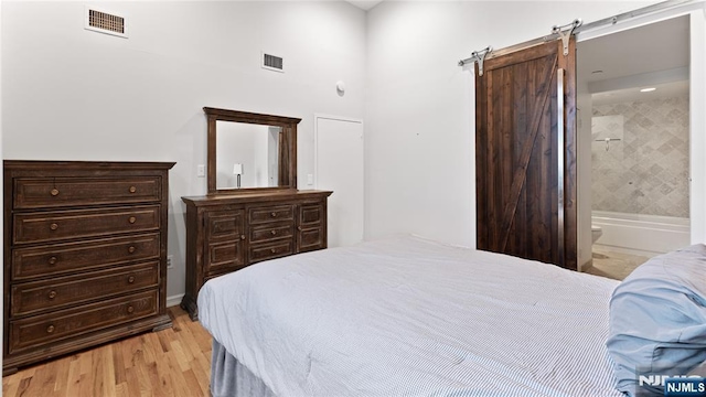 bedroom with ensuite bathroom, a barn door, and light wood-type flooring