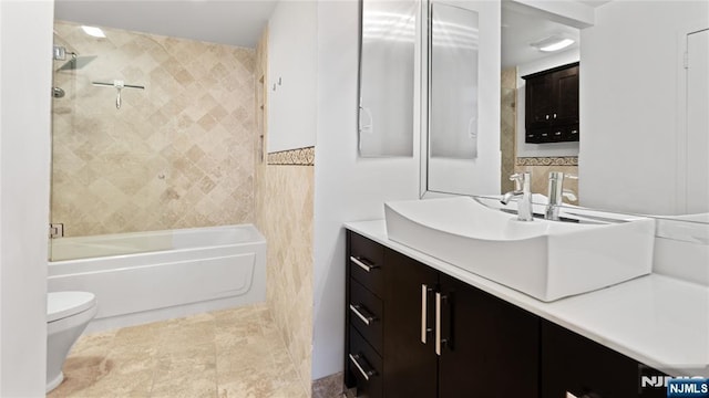 full bathroom featuring vanity, tiled shower / bath, tile walls, and toilet