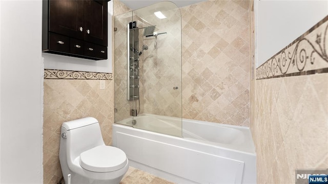 bathroom featuring tiled shower / bath, toilet, and tile walls