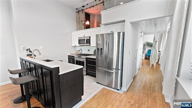 kitchen featuring a kitchen bar, sink, white cabinetry, a towering ceiling, and stainless steel appliances