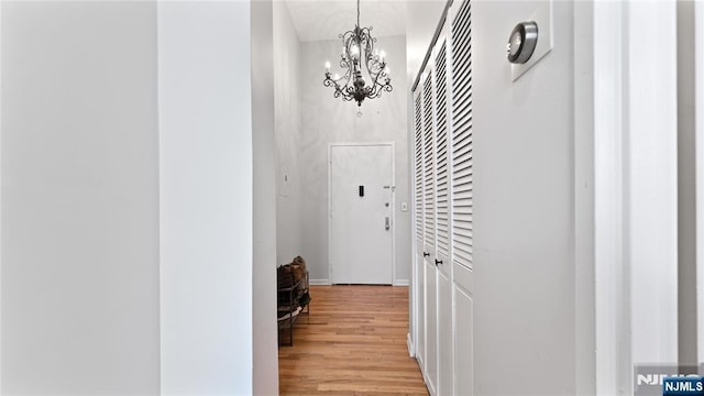 corridor with a towering ceiling, a chandelier, and light wood-type flooring