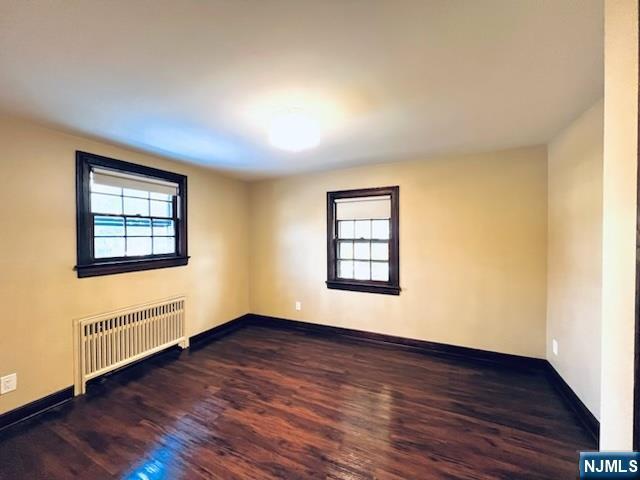 empty room featuring radiator heating unit and dark hardwood / wood-style floors