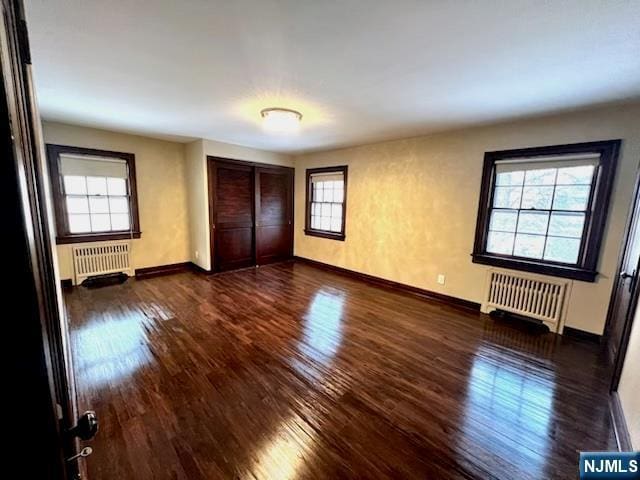 unfurnished bedroom with dark wood-type flooring, radiator heating unit, and a closet