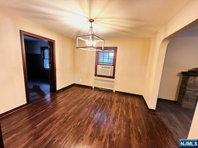 unfurnished dining area featuring dark hardwood / wood-style floors, radiator heating unit, a chandelier, and cooling unit