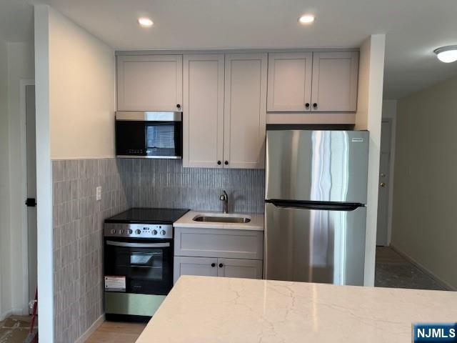 kitchen with stainless steel appliances, gray cabinets, light stone countertops, and sink