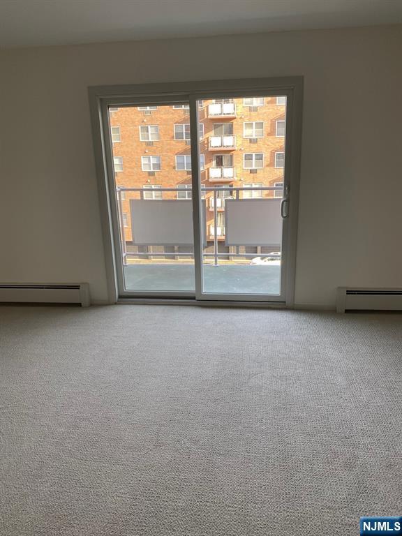 unfurnished room featuring carpet floors and a baseboard heating unit