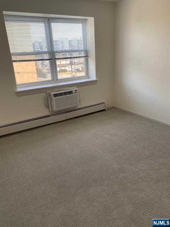 spare room featuring carpet, an AC wall unit, and baseboard heating