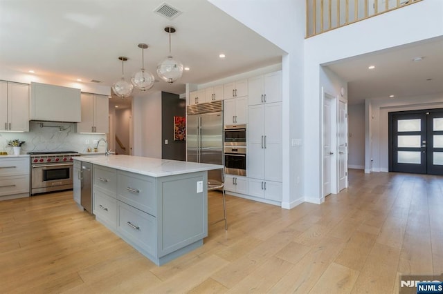 kitchen featuring high end appliances, pendant lighting, light hardwood / wood-style flooring, and an island with sink