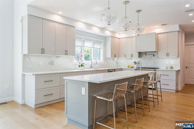 kitchen with sink, a kitchen bar, hanging light fixtures, a kitchen island with sink, and light hardwood / wood-style floors