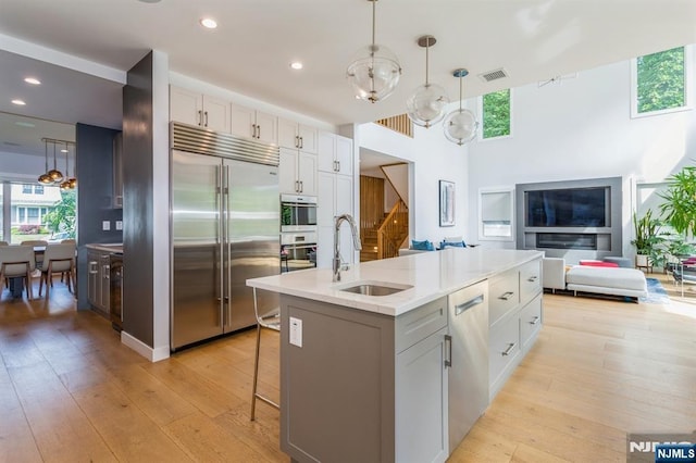 kitchen featuring sink, white cabinetry, stainless steel appliances, a center island with sink, and decorative light fixtures