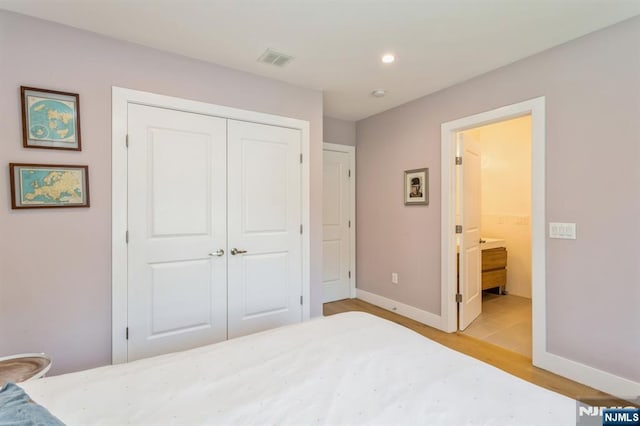 bedroom with ensuite bathroom, light hardwood / wood-style floors, and a closet