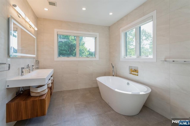 bathroom featuring tile walls, vanity, a washtub, and a wealth of natural light