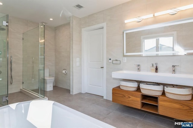 bathroom featuring toilet, tile patterned flooring, tile walls, and shower with separate bathtub