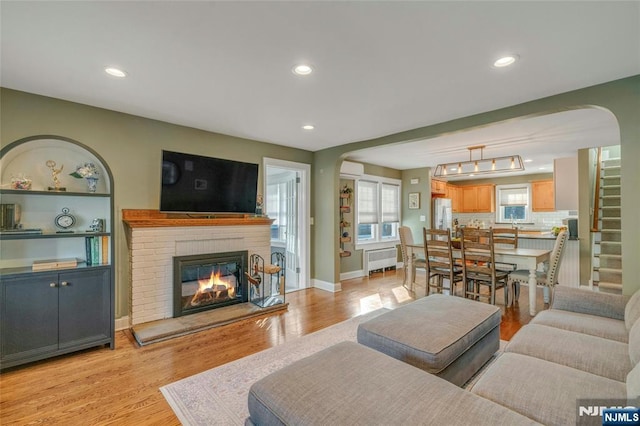 living room featuring radiator, built in shelves, a brick fireplace, and light wood-type flooring