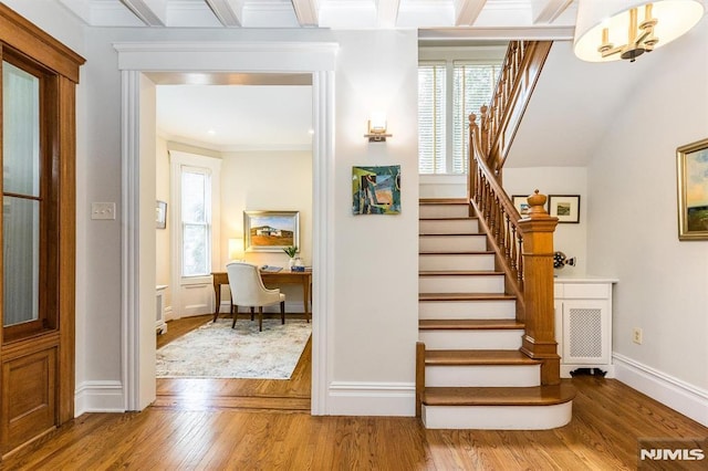 stairway with crown molding, hardwood / wood-style flooring, plenty of natural light, and beam ceiling