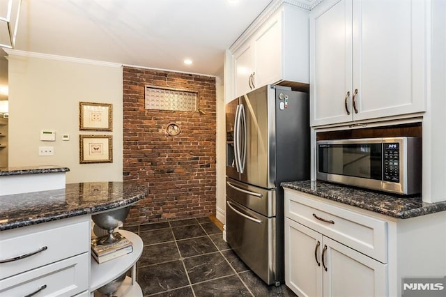 kitchen featuring stainless steel appliances, dark stone counters, white cabinets, and brick wall