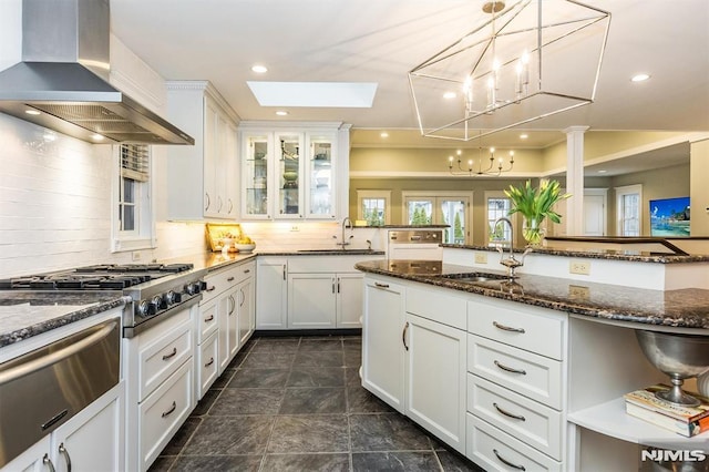 kitchen with island exhaust hood, dark stone counters, sink, and white cabinets