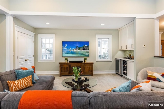 carpeted living room featuring bar, beverage cooler, and ornate columns