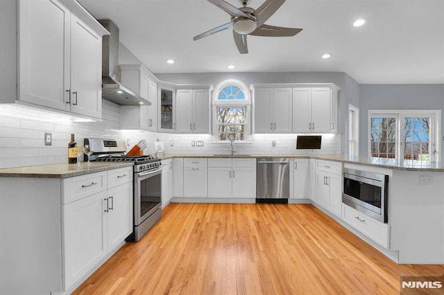 kitchen featuring a sink, tasteful backsplash, stainless steel appliances, a peninsula, and wall chimney exhaust hood