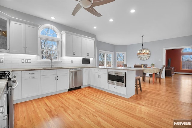 kitchen with backsplash, appliances with stainless steel finishes, a peninsula, white cabinets, and a sink