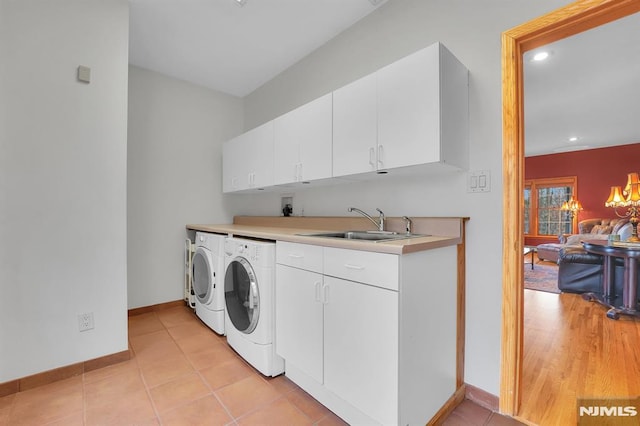 laundry area featuring light tile patterned floors, baseboards, cabinet space, a sink, and washer and clothes dryer