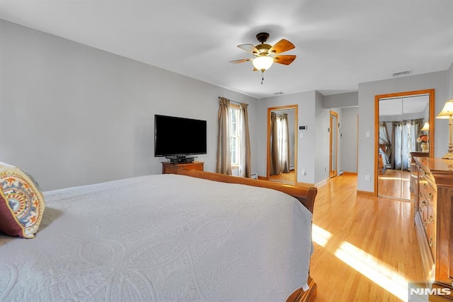 bedroom featuring visible vents, two closets, ceiling fan, baseboards, and light wood-type flooring