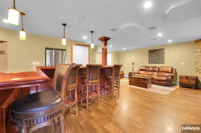 bar with decorative light fixtures, recessed lighting, freestanding refrigerator, wood finished floors, and a bar