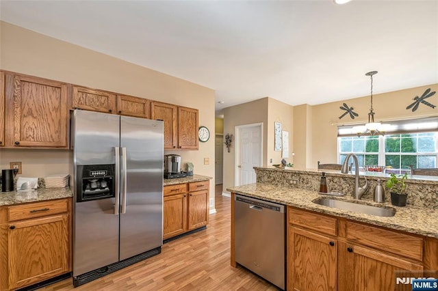 kitchen featuring sink, appliances with stainless steel finishes, hanging light fixtures, light stone counters, and light hardwood / wood-style floors