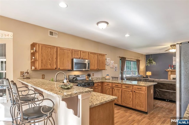 kitchen featuring light hardwood / wood-style flooring, appliances with stainless steel finishes, a kitchen breakfast bar, kitchen peninsula, and light stone countertops