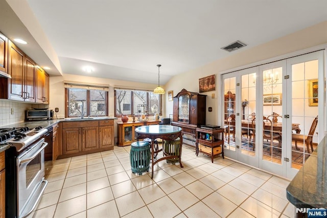 kitchen featuring sink, backsplash, hanging light fixtures, light tile patterned floors, and gas range