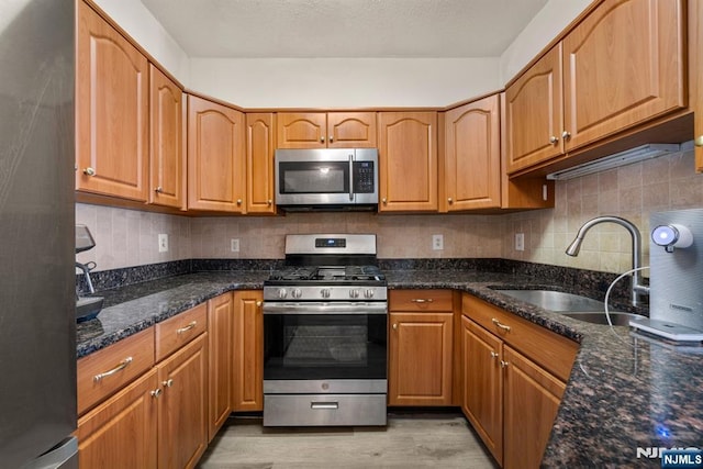 kitchen with tasteful backsplash, sink, dark stone countertops, stainless steel appliances, and light hardwood / wood-style flooring