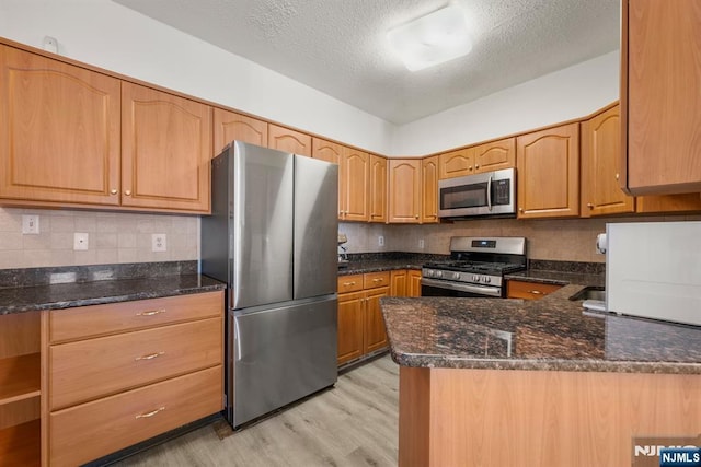 kitchen featuring a textured ceiling, light hardwood / wood-style flooring, dark stone countertops, stainless steel appliances, and decorative backsplash