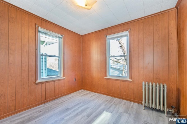 spare room featuring radiator, light hardwood / wood-style floors, and wood walls