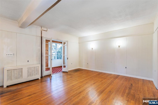 unfurnished room with wood-type flooring, radiator, and beam ceiling