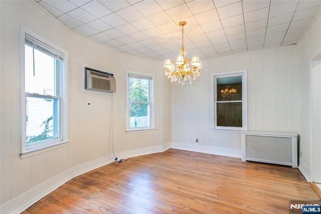 spare room with a wall mounted AC, a wealth of natural light, radiator, and light wood-type flooring