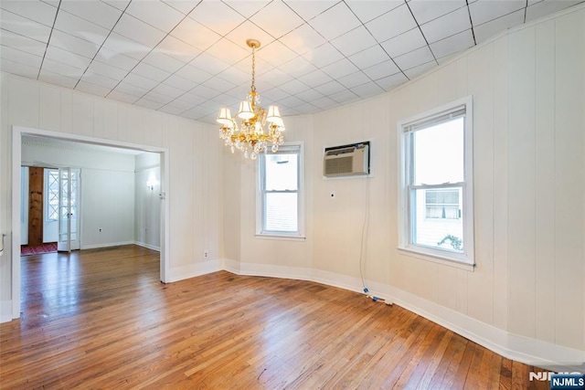 spare room featuring wood-type flooring, a wall mounted air conditioner, and an inviting chandelier