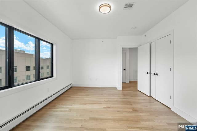 unfurnished bedroom with light wood-type flooring and a baseboard heating unit