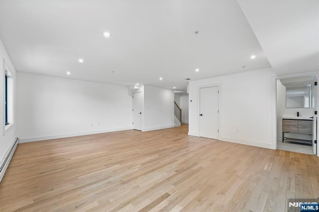 unfurnished living room with a baseboard heating unit and light hardwood / wood-style flooring