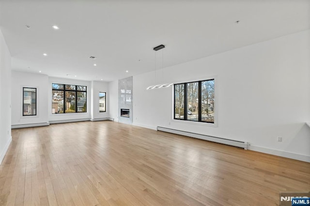 unfurnished living room featuring a baseboard heating unit, light hardwood / wood-style floors, and a large fireplace