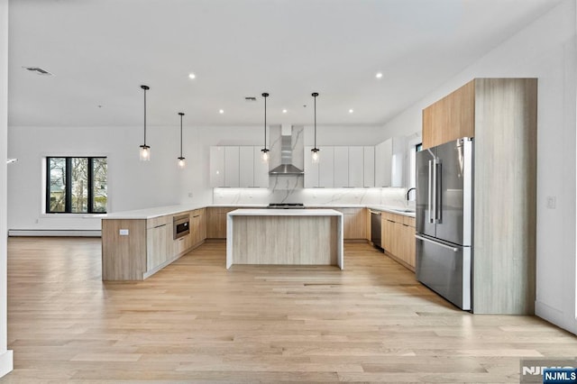 kitchen featuring wall chimney exhaust hood, hanging light fixtures, appliances with stainless steel finishes, a kitchen island, and white cabinets