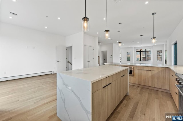 kitchen featuring a baseboard heating unit, a spacious island, light stone counters, light hardwood / wood-style floors, and light brown cabinets